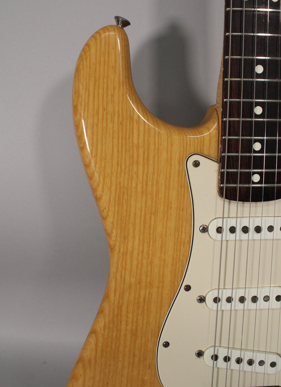 Close-up of the guitar's upper body, showing the light wood grain, cream pickguard, three single-coil pickups, and rosewood fretboard.