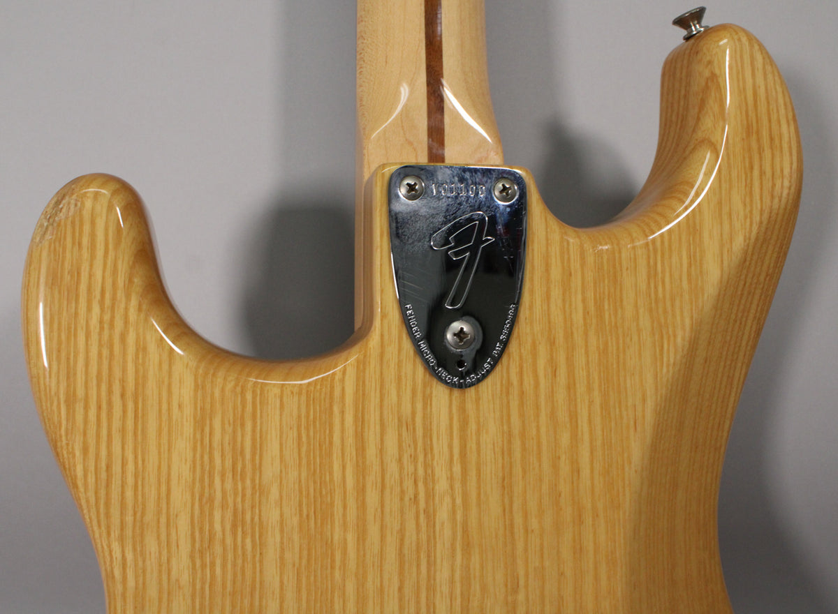 The back of a light wood guitar body with a chrome neck plate, showing the neck joint and upper horn with a strap button.