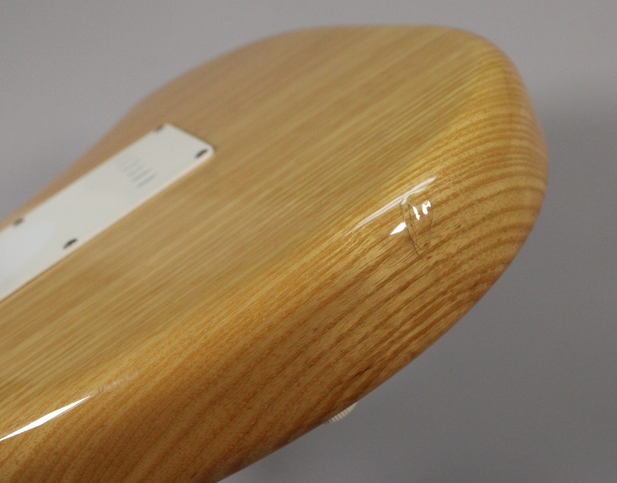 Close-up of the guitar's natural wood body, showing a white tremolo cover and a visible ding in the glossy finish near the lower bout.