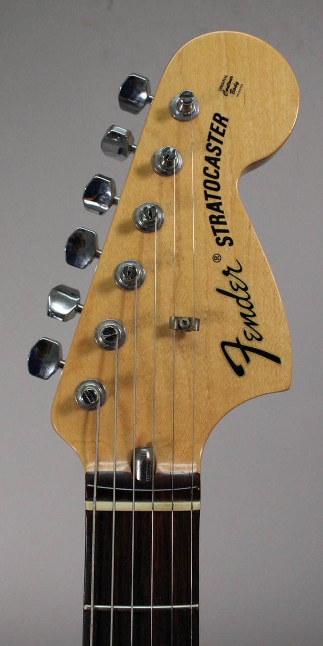 The guitar's light wood headstock, with six chrome tuners and two string trees, meets a dark rosewood fingerboard.
