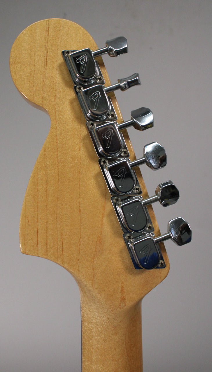 The back of a light wood headstock and neck, angled left, with six chrome tuners in a row down the right side.