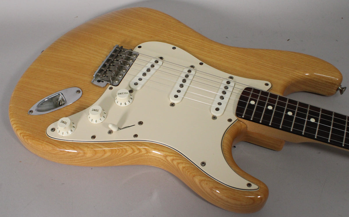 Light woodgrain Stratocaster body with a white pickguard, three single-coil pickups, and a rosewood fingerboard, viewed from above.