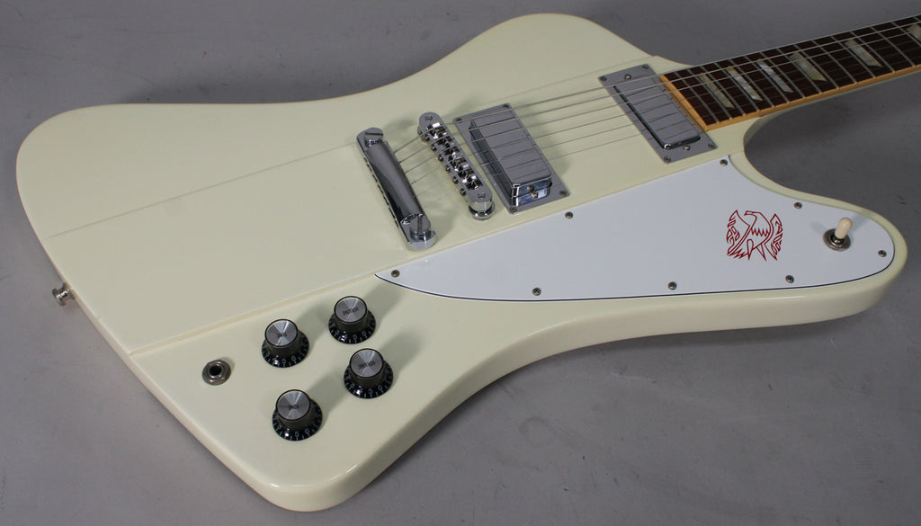 Close-up of the guitar's body, showing the creamy white finish, chrome hardware, white pickguard with red bird graphic, and four black control knobs.