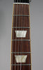 Close-up of the dark brown fretboard with two trapezoidal mother-of-pearl inlays, silver frets, and six strings.