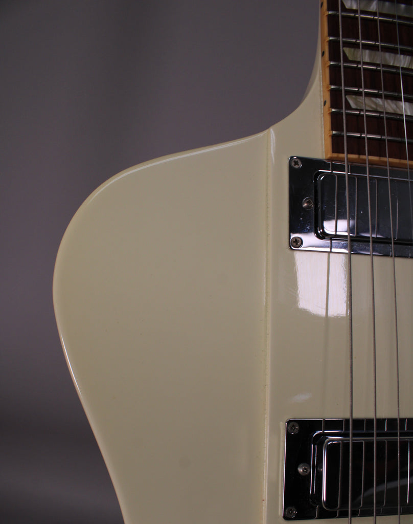Close-up of the upper body of an off-white guitar, showing two chrome humbucker pickups and a bound fretboard with block inlays.