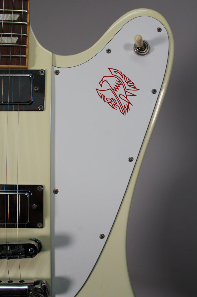 Close-up of the guitar's upper body, showing the white pickguard with a red bird graphic, a cream toggle switch, and chrome pickups.