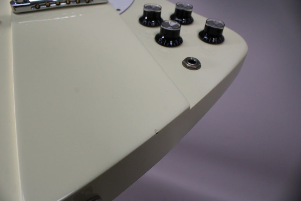 Close-up of the guitar's lower body, showing the off-white finish, four black control knobs, input jack, and a small chip on the edge.