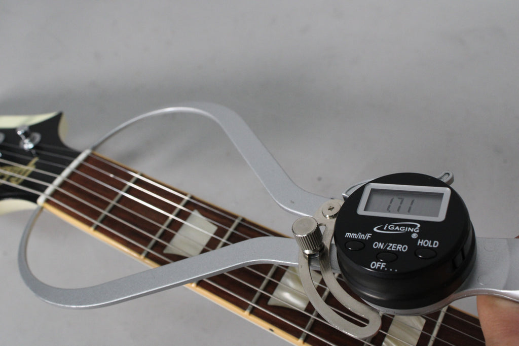 A digital caliper measures the guitar's nut width at 1.71 inches, with the headstock and fretboard visible.