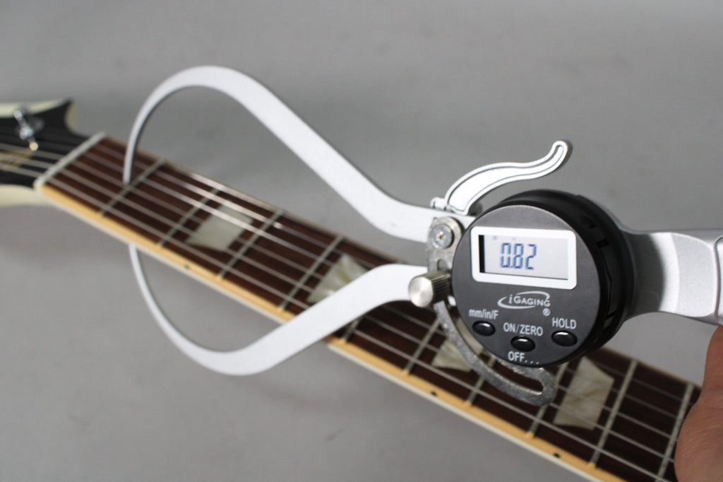 A digital fret height gauge measures the guitar's fretboard, showing a reading of 0.82, with trapezoid inlays visible.