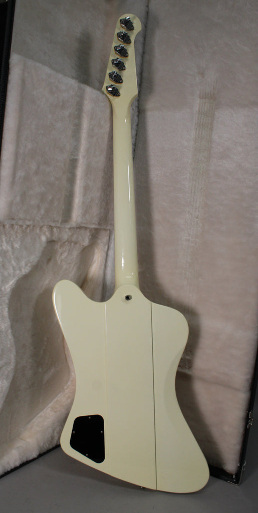 The back of an off-white guitar with a black control cavity cover, six tuners, and a visible strap button, resting in a case.