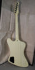 The back of an off-white guitar with a black control cavity cover, six tuners, and a visible strap button, resting in a case.