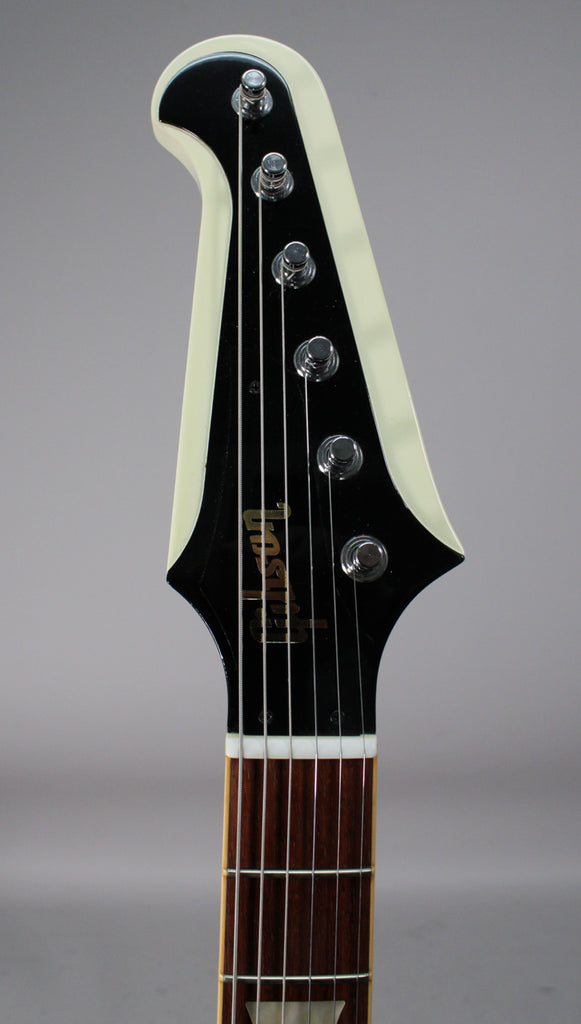 Close-up of the Firebird's headstock, showing the black face with gold lettering, chrome tuners, and a white binding.