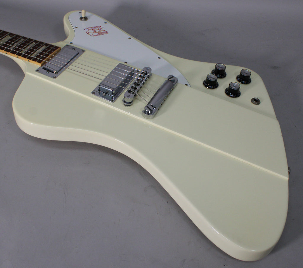 Angled view of an off-white electric guitar with chrome hardware, four black control knobs, and a white pickguard with a red bird graphic.