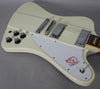 Close-up of the guitar's body, showing the off-white finish, white pickguard with red bird graphic, four black control knobs, and chrome hardware.