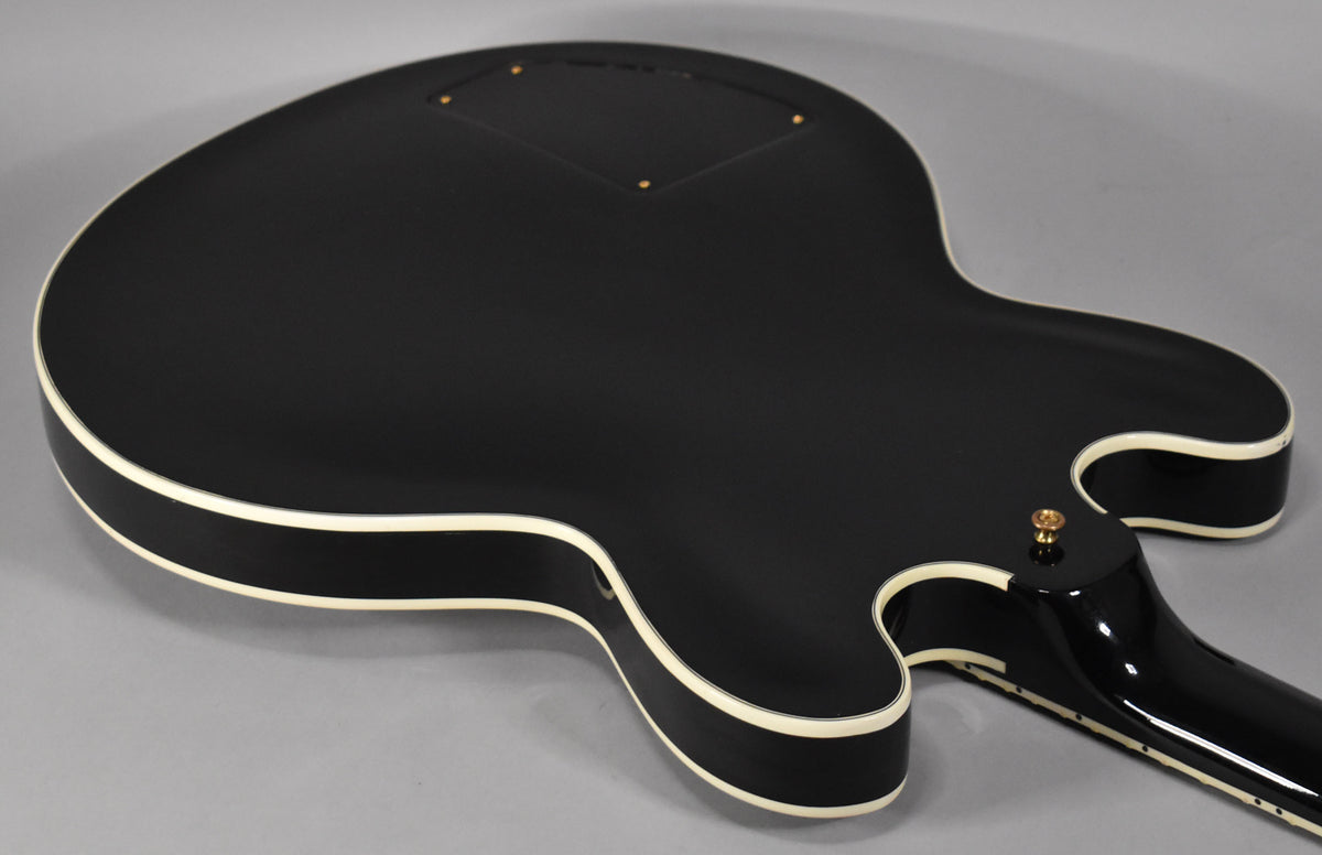 The back of an ebony guitar with a matte finish and cream binding, showing the control cavity cover and neck joint.