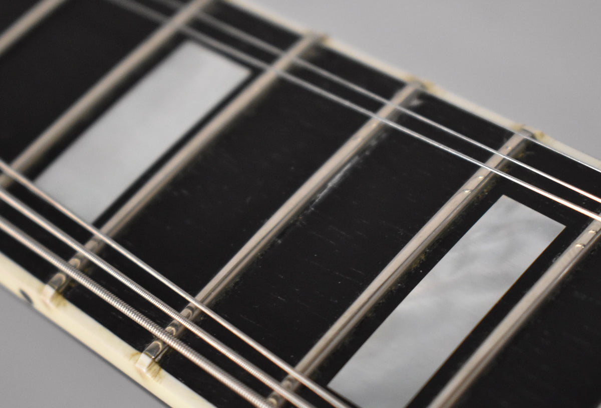 Close-up of the ebony fretboard with mother-of-pearl block inlays, showing light wear and some grime along the frets and binding.