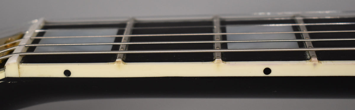 Close-up of the ebony fretboard and white binding, showing the first few frets, mother-of-pearl block inlays, and side dots.