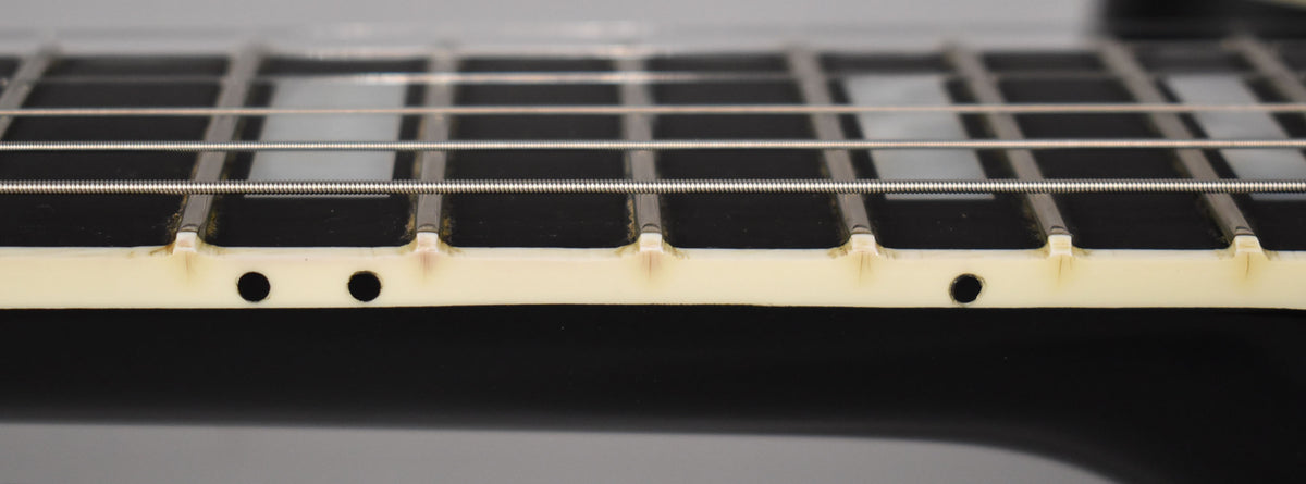 Close-up of the ebony fretboard and cream binding, showing light wear and grime around the frets and two side dot markers.