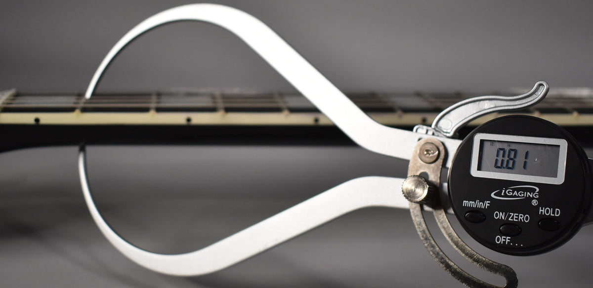 A digital caliper measures the guitar's neck relief, showing 0.81, with the ebony fretboard and frets visible in the background.