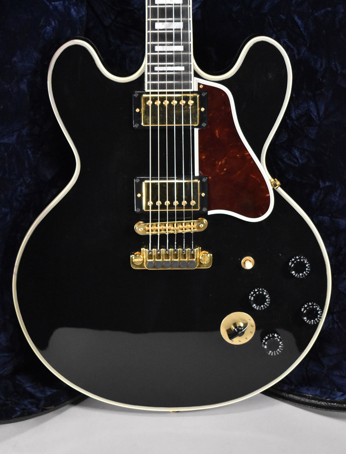 Full-frame view of a glossy black hollow-body electric guitar with gold hardware, a tortoiseshell pickguard, and white binding.