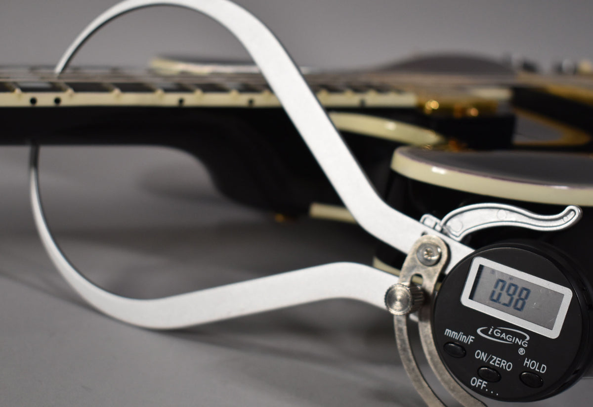 A digital caliper measures the fret height at 0.98mm on the ebony guitar's bound fretboard, showing light fret wear.