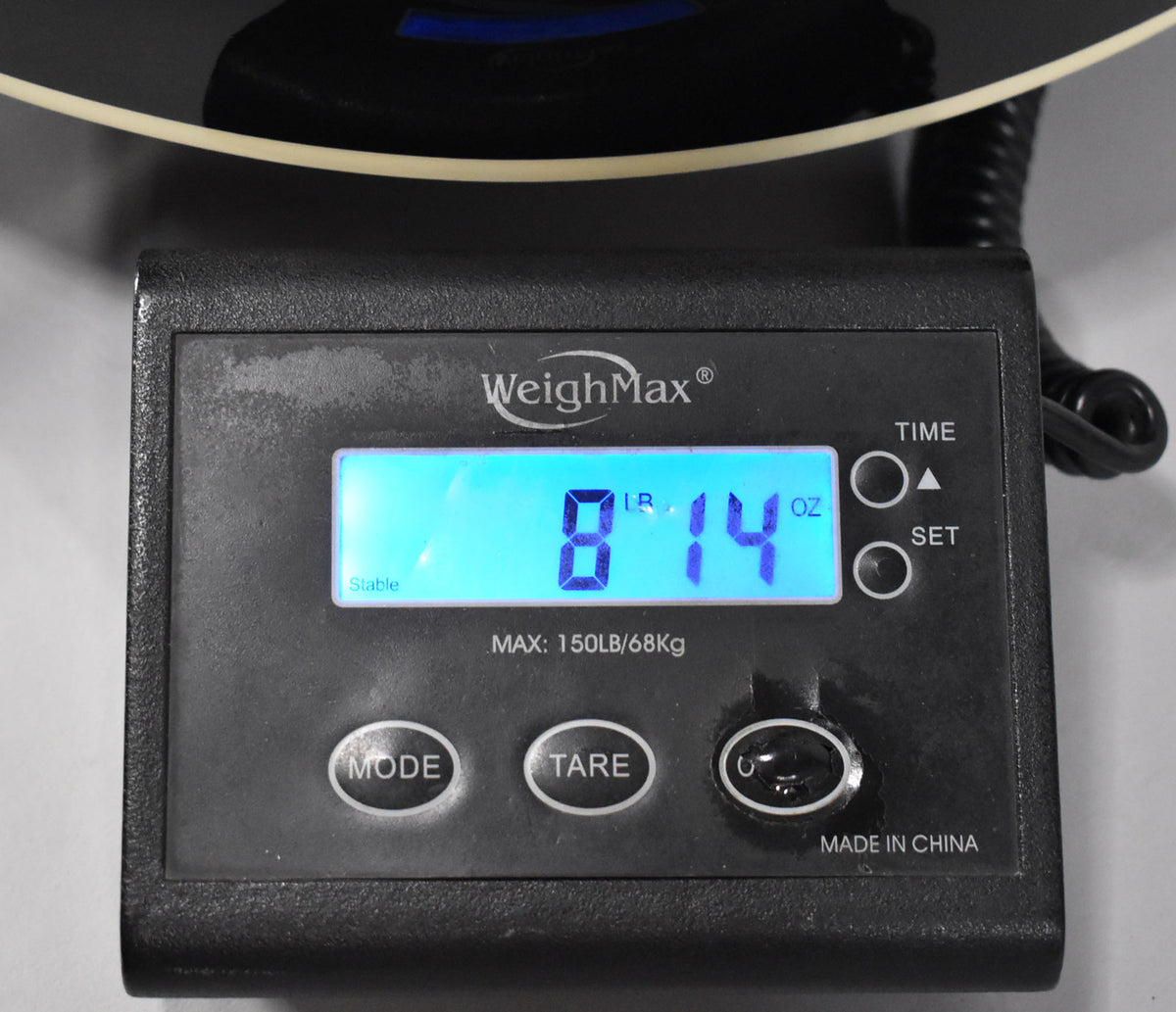 Close-up of a digital scale displaying "8 LB 14 OZ" in blue, with the guitar's black body and cream binding visible above.