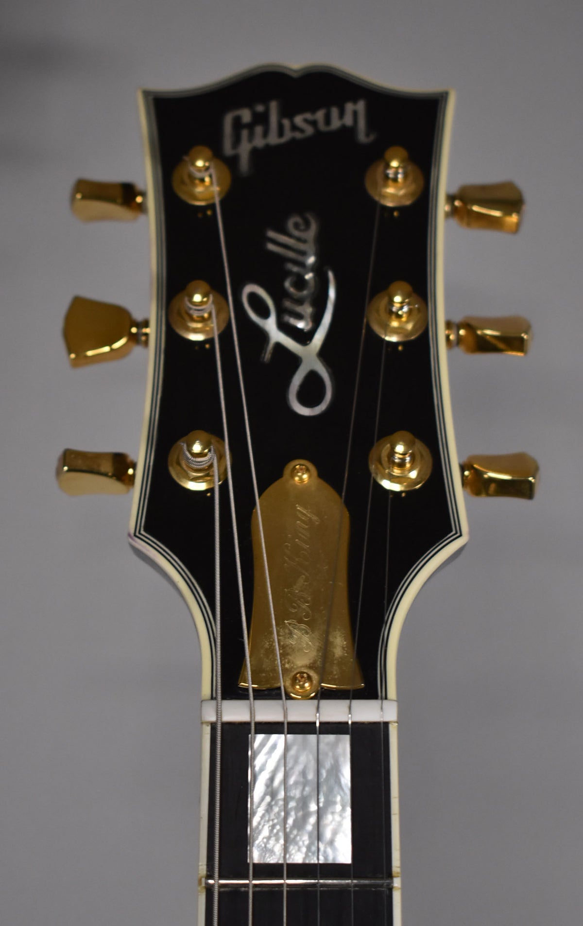 Close-up of the ebony headstock with gold tuners, a gold truss rod cover, and mother-of-pearl "Lucille" inlay.