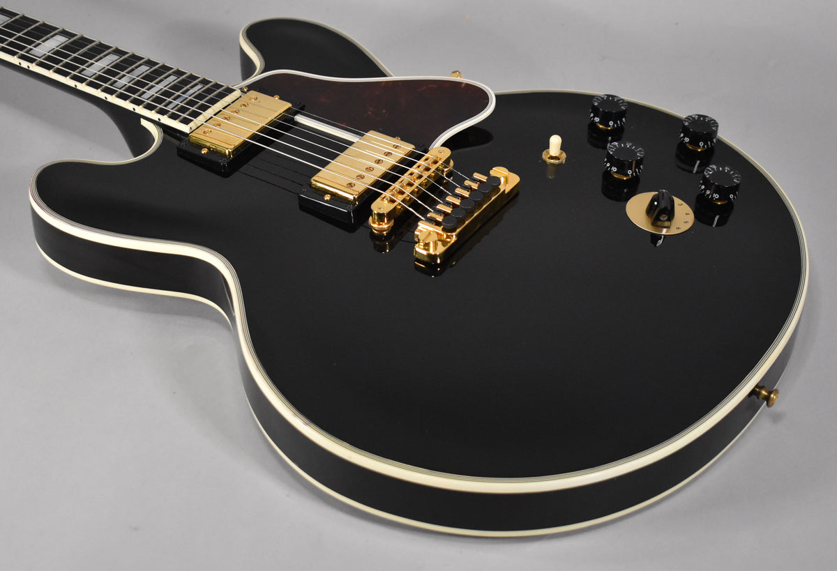 Ebony gloss guitar body with white binding, gold hardware, black knobs, and a dark tortoiseshell pickguard, viewed from above.
