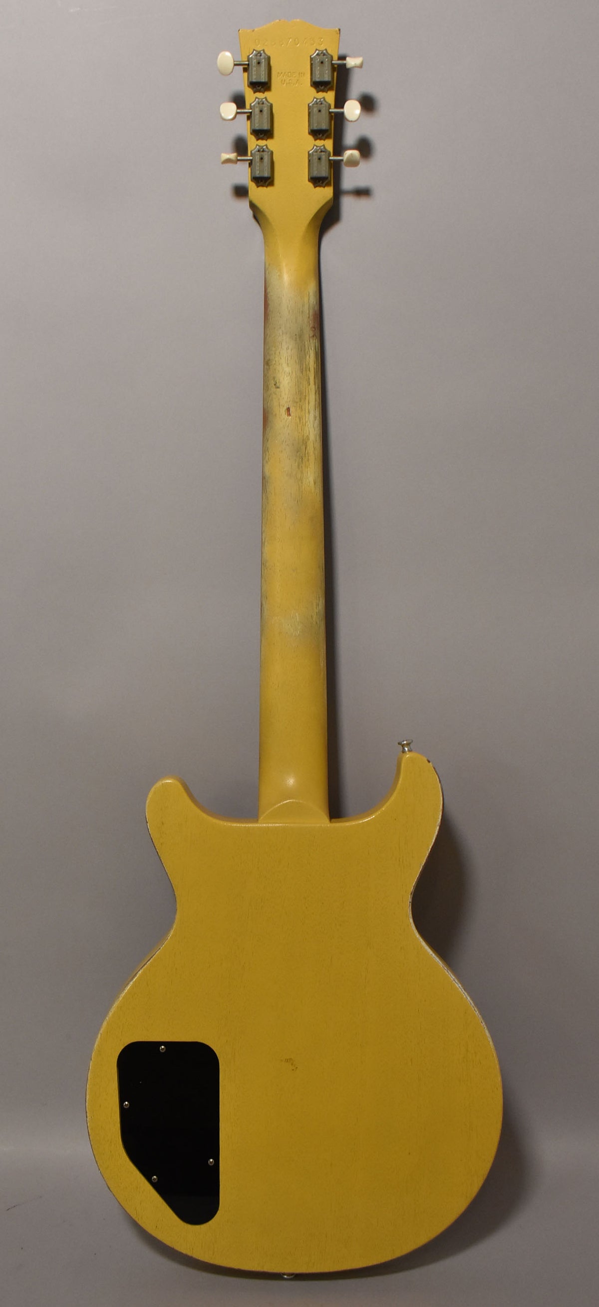 Full back view of a faded TV yellow guitar with a worn neck, six white-button tuners, and a black control cavity cover.