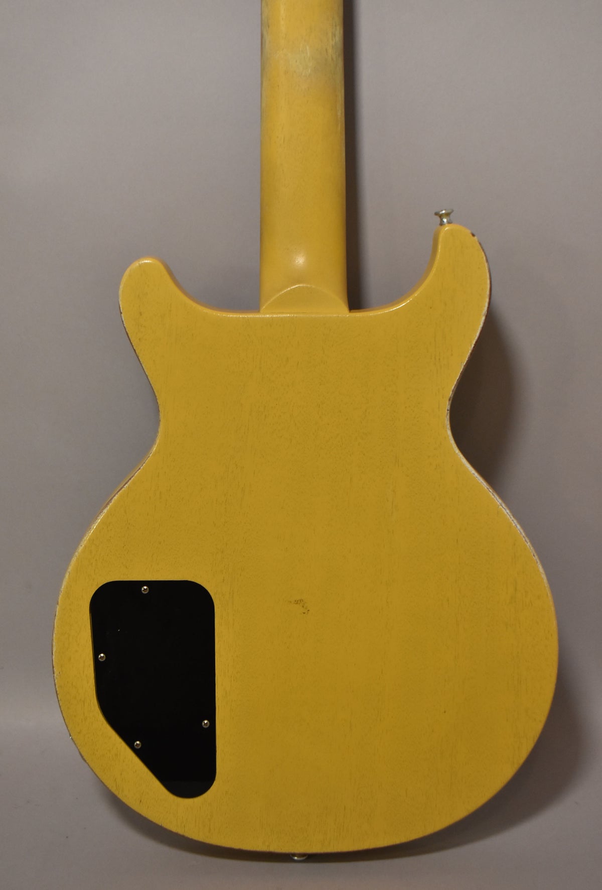 Rear view of a faded TV yellow double-cutaway electric guitar with a black control cavity cover and visible wear on the neck and body edges.