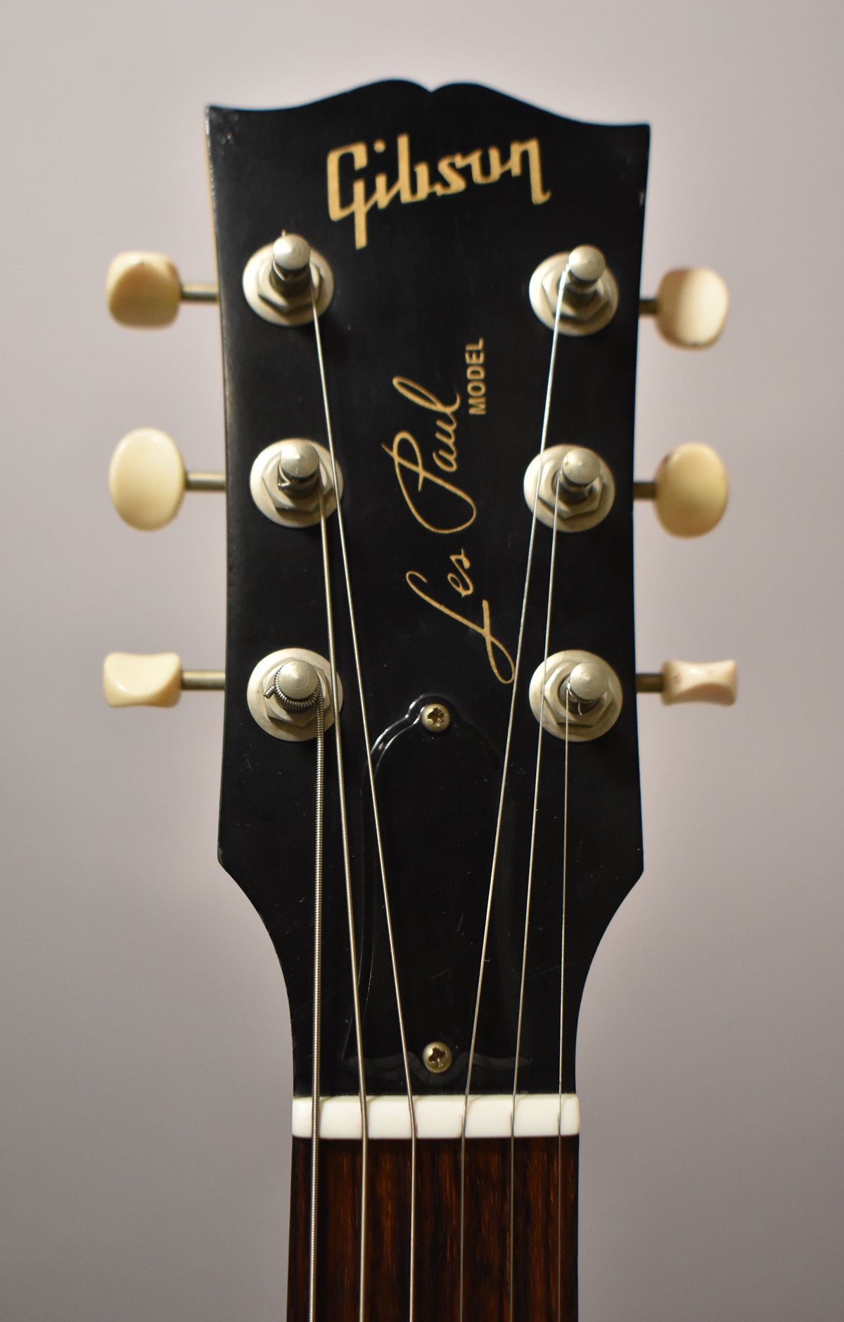 Close-up of the black headstock with cream tuners, showing some wear on the top edge and a dark rosewood fretboard.