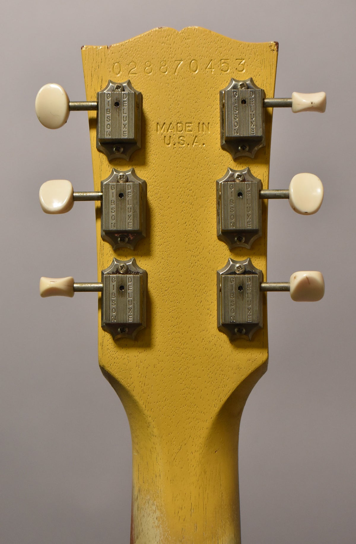The back of a faded TV Yellow headstock with six cream-buttoned tuners, showing wear and a serial number stamped at the top.