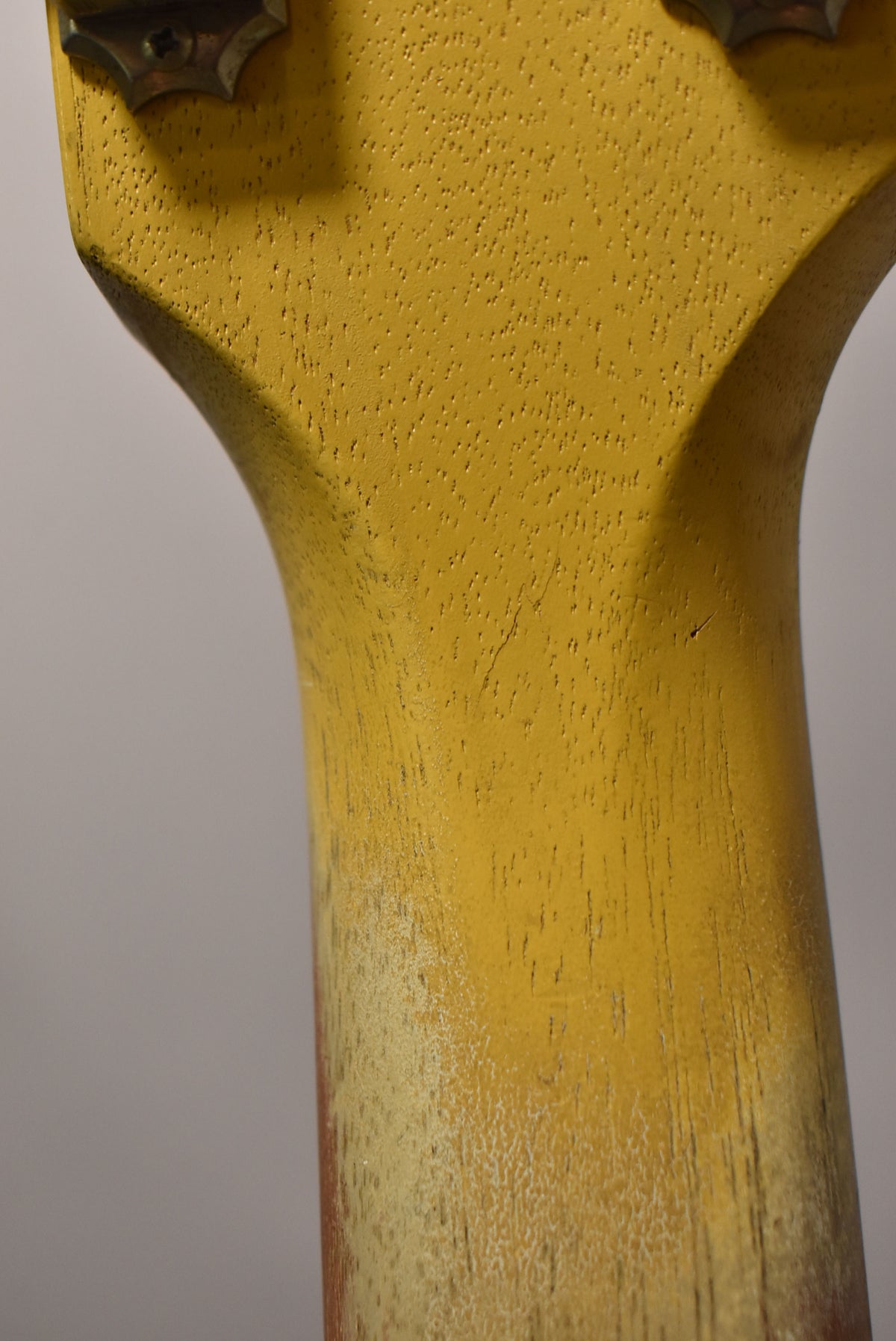 Close-up of the TV yellow headstock and neck heel, showing heavy finish wear and checking, revealing the wood grain below.