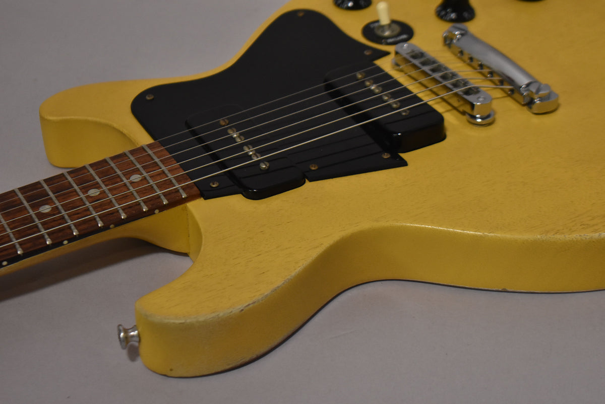 Upper body of a faded TV yellow double-cut guitar with black P90 pickups, a tune-o-matic bridge, and visible wear on the lower horn.