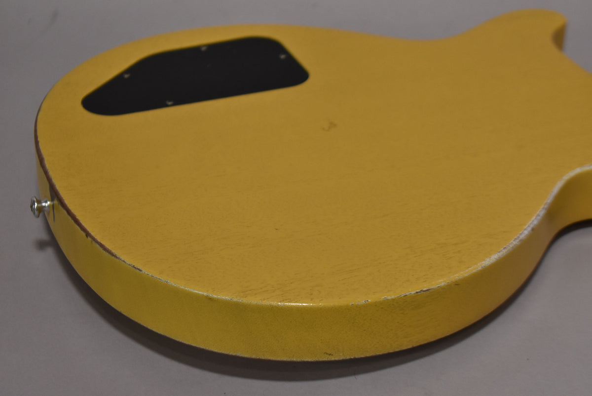 The back of the faded TV yellow guitar body, showing a black control cavity cover and wear along the edges.