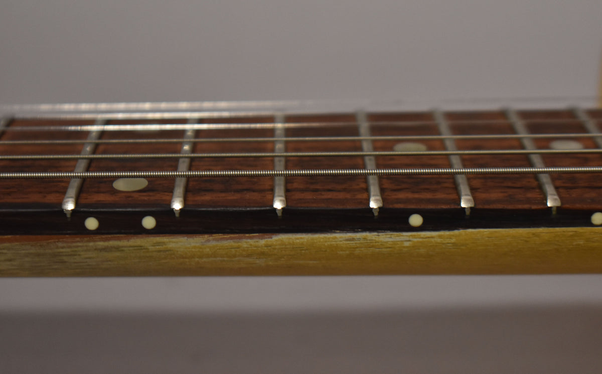 Close-up of the guitar's dark rosewood fretboard with oval inlays and side dots, showing light wear on the faded TV yellow neck.