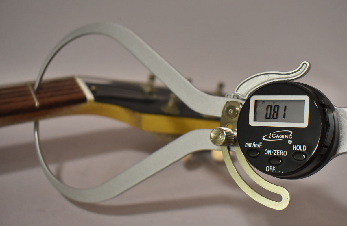 A digital caliper measures the guitar's nut width at 0.81, with the faded TV yellow headstock and fretboard visible behind it.