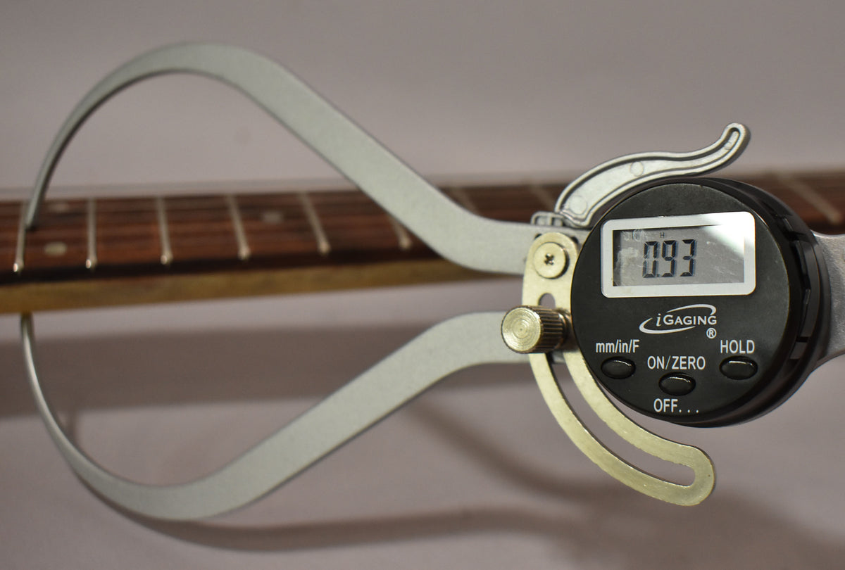 A digital caliper measures the guitar's fret height at 0.93, with the dark rosewood fretboard and frets visible.