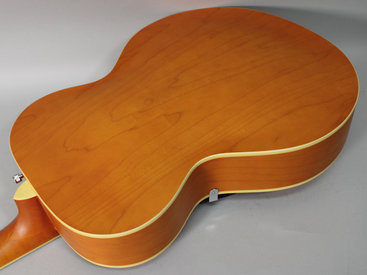 The back of a natural matte archtop guitar, showing the light wood grain, cream binding, and a strap button on the lower bout.