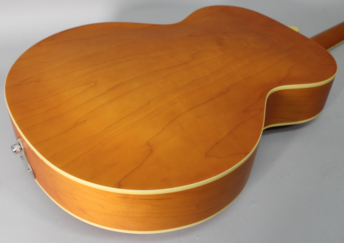 The guitar's natural matte finish back and side are visible, with light wood grain and cream binding, and a chrome output jack.