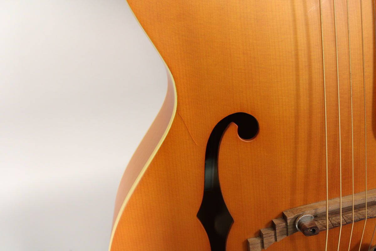 Close-up of the natural matte archtop guitar body, showing the f-hole, strings, and a small crack near the upper bout.