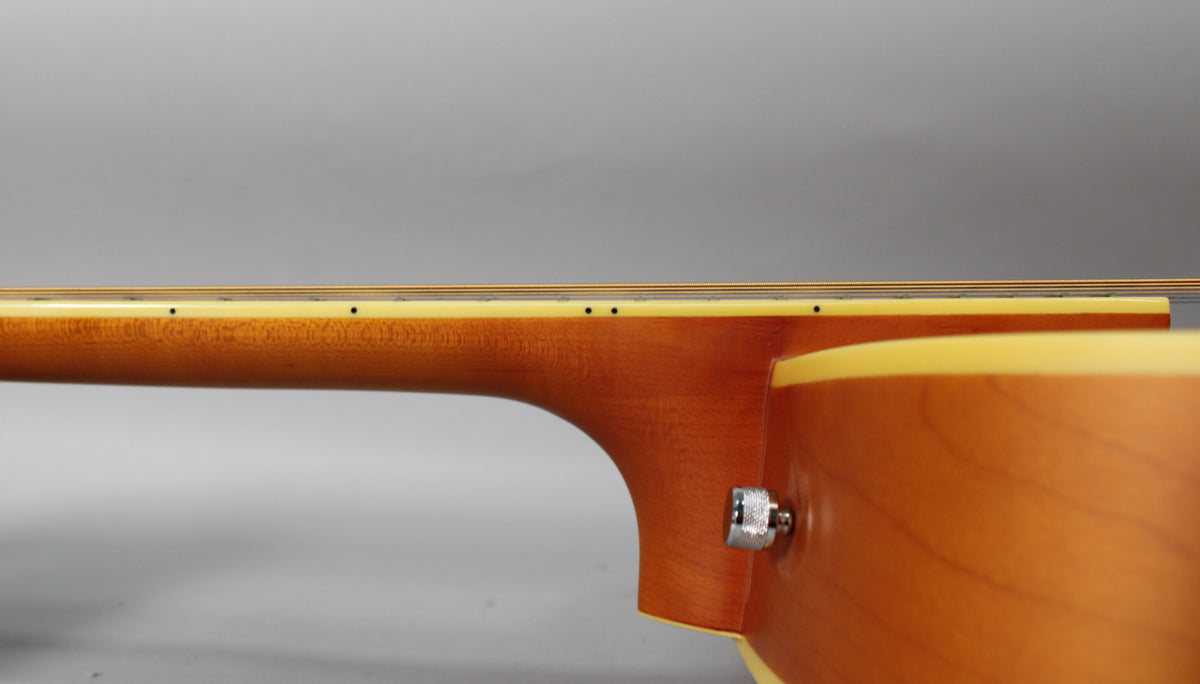The guitar's neck and upper body are visible from the side, showing a natural matte finish and a chrome strap button.