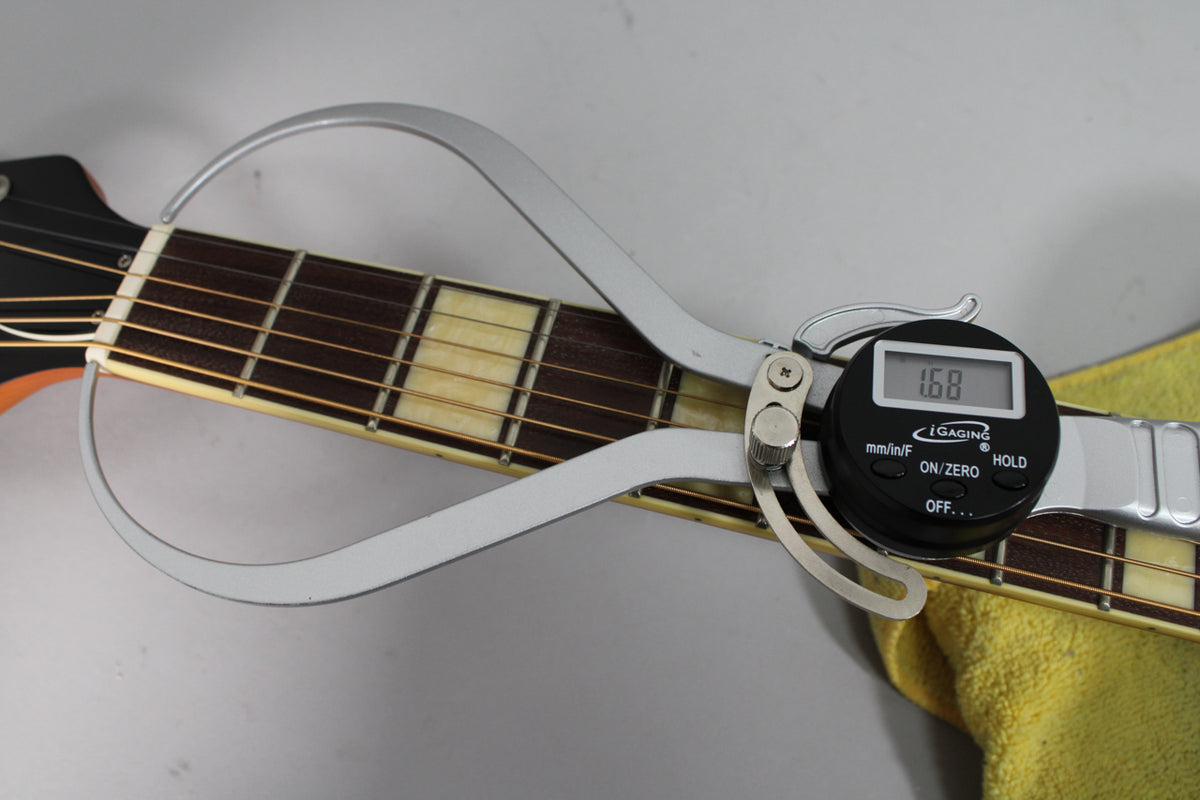 A digital caliper measures the nut width of the guitar's dark fretboard with rectangular cream inlays, showing "1.68".