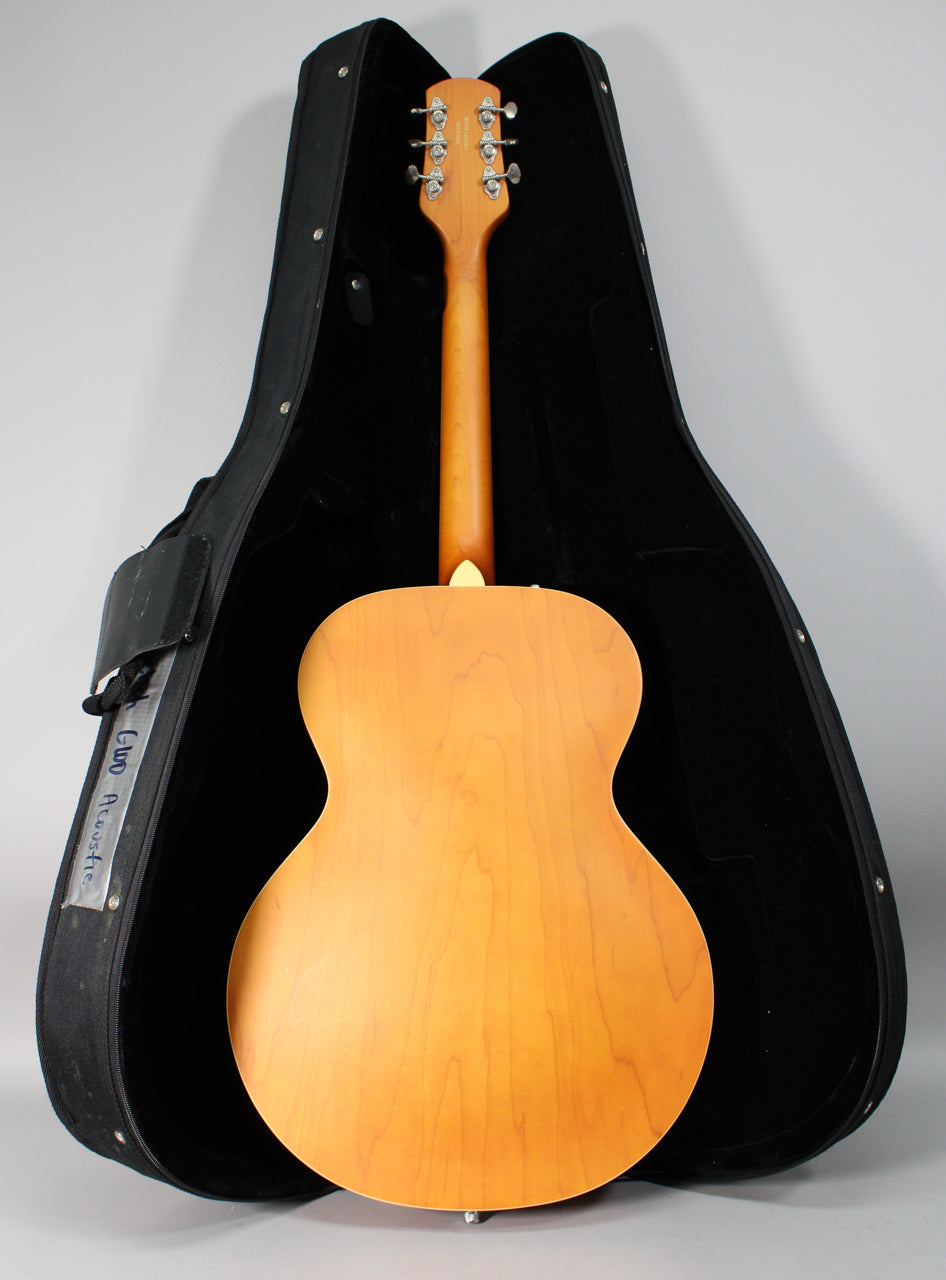 The guitar's natural matte finish back and neck are visible, with six chrome tuners on the headstock, resting in a black hard case.