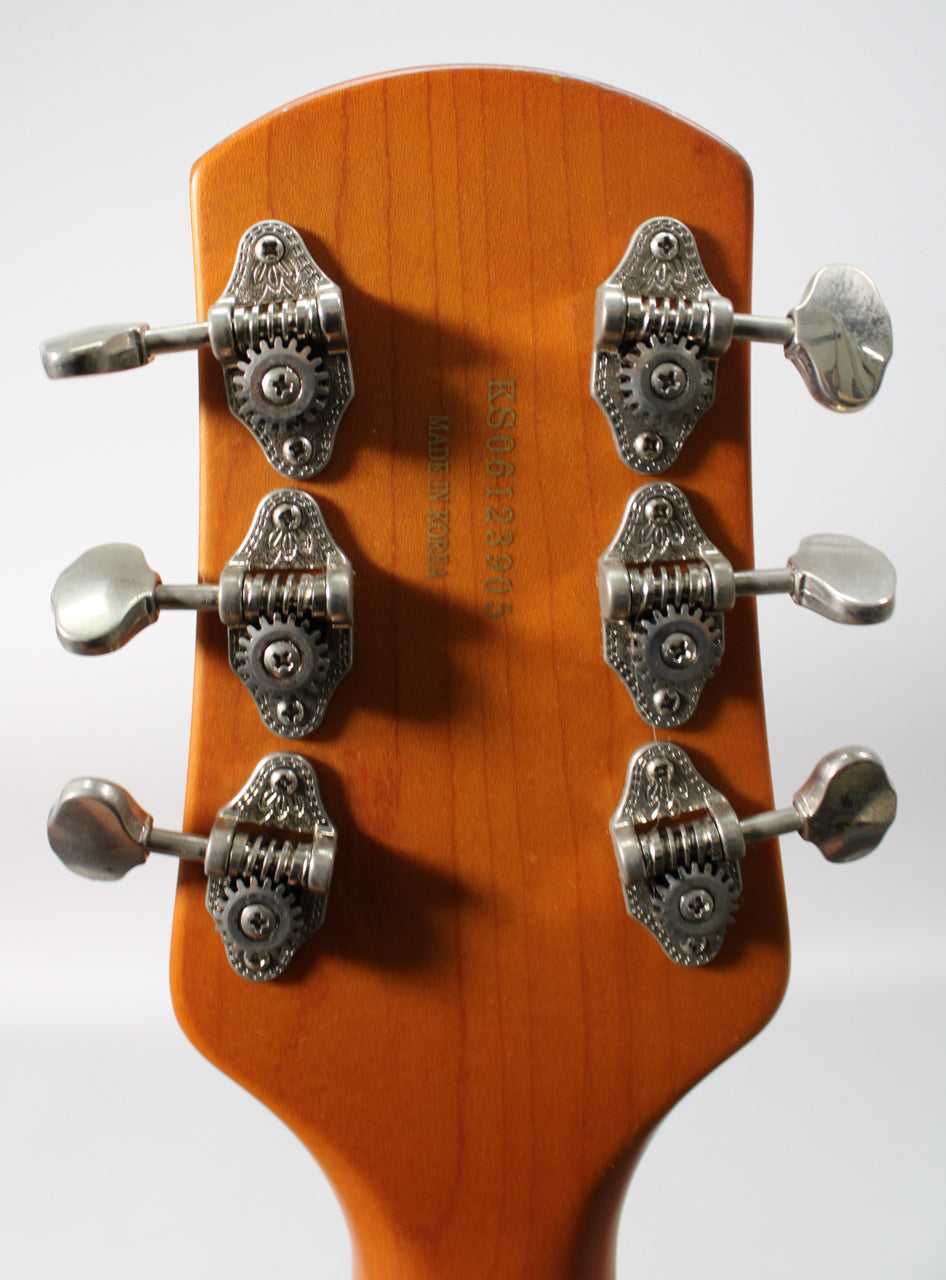 The back of a light brown matte headstock with six ornate silver tuners, three on each side, and a serial number.