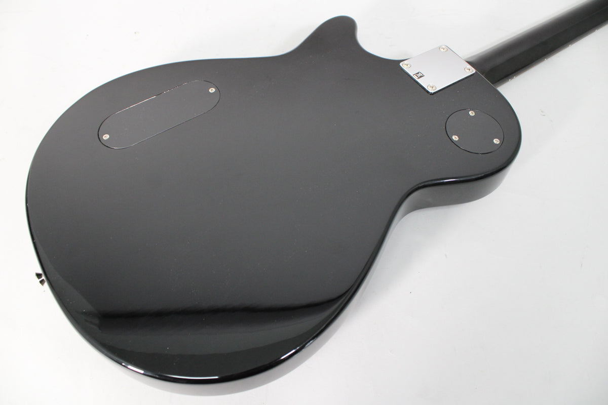 The back of a black electric guitar, showing a rectangular control plate, a round control plate, and a chrome neck plate.