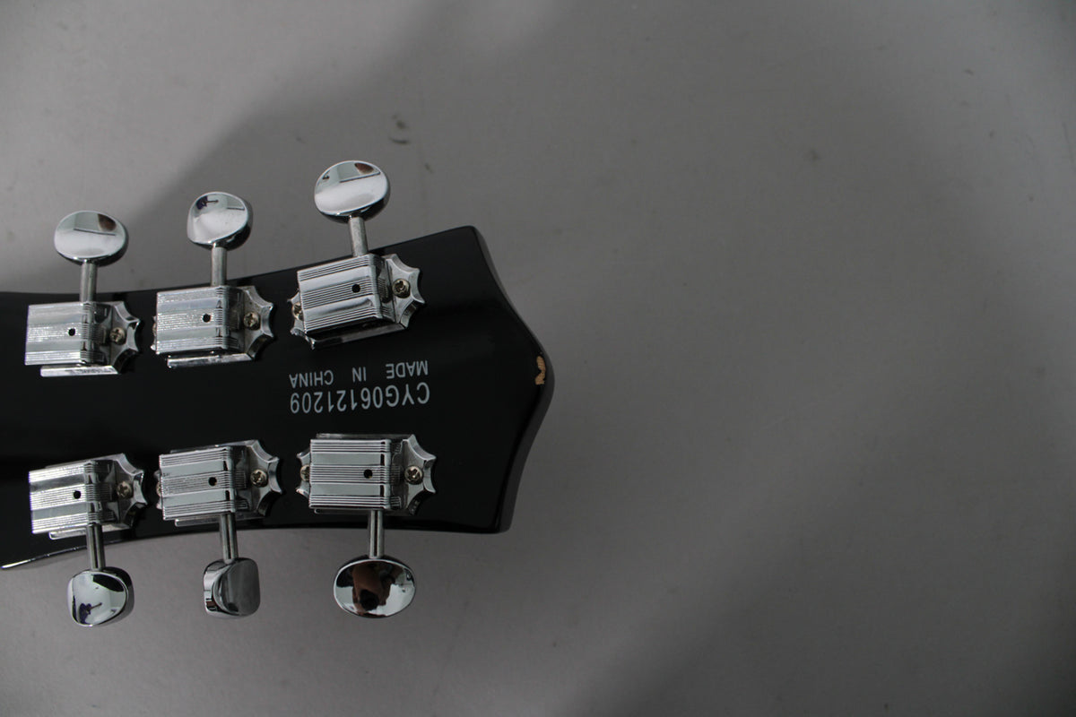 Rear view of the black headstock with six chrome tuners, three on each side, and a small chip on the top right edge.