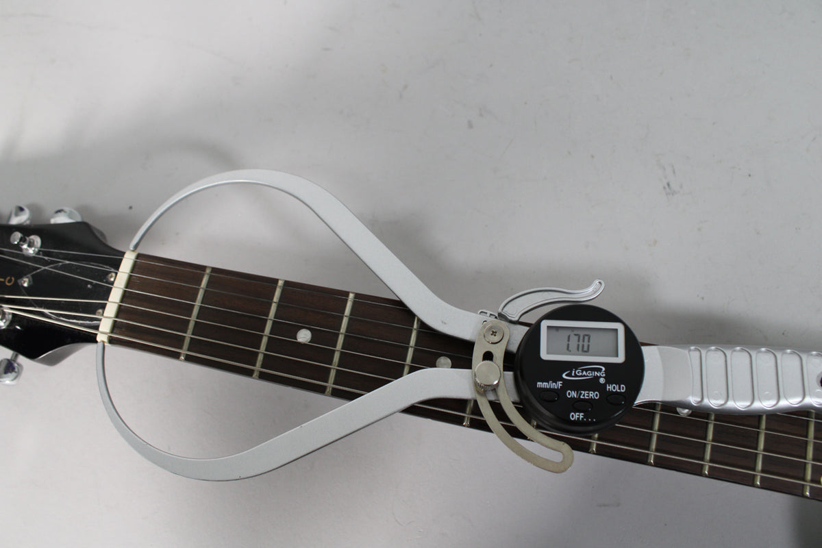 The guitar's dark fretboard and headstock are measured by a silver digital caliper showing "1.70" on its screen.