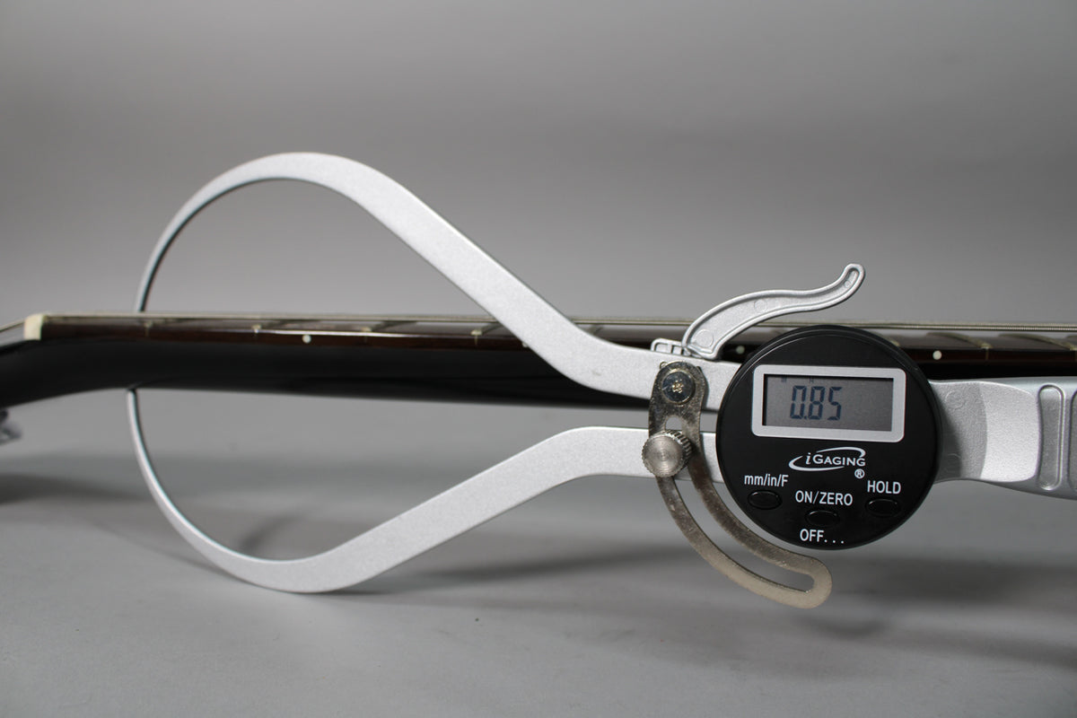 A digital caliper measures the guitar's dark brown fretboard, showing a reading of 0.85, with light fret markers visible.