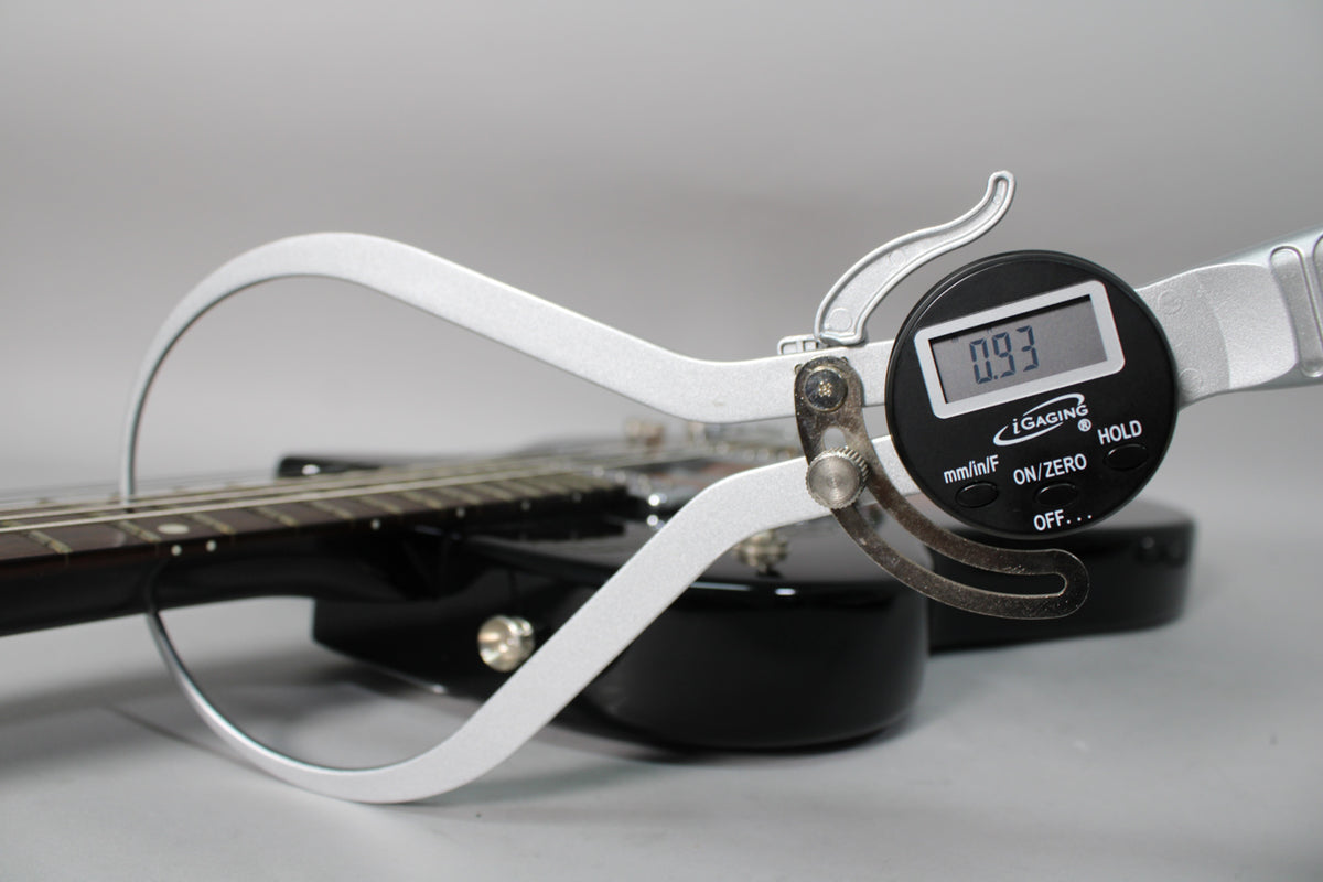 A digital caliper measures the string height at the 12th fret of the black electric guitar, displaying "0.93".
